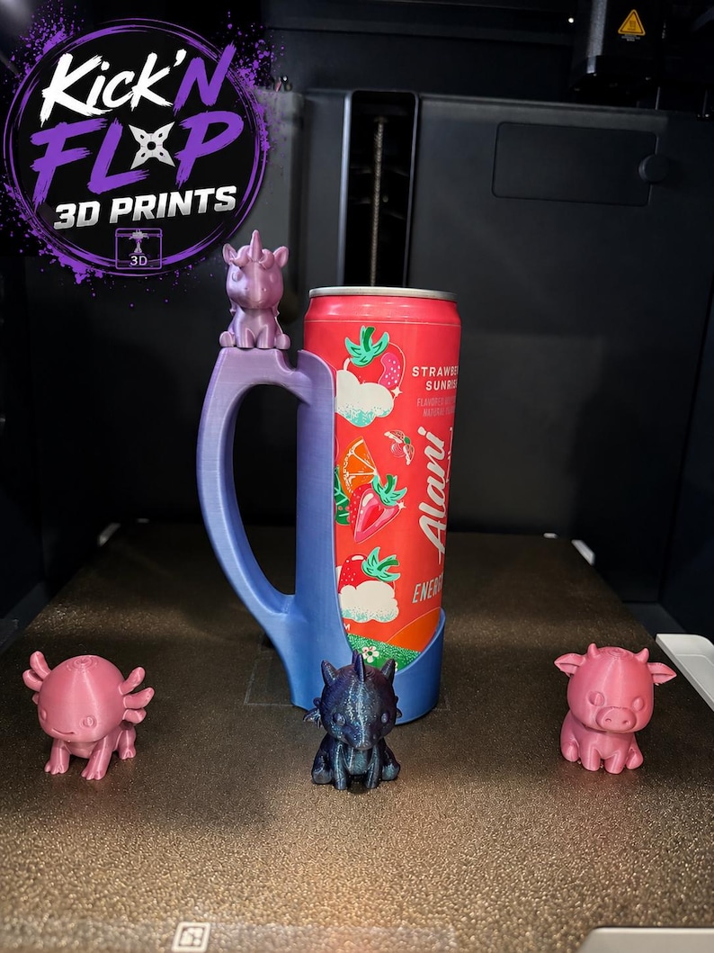 May include: A 3D-printed blue gradient can holder featuring a unicorn figure on the handle, holding a red Alani Nu Strawberry Sunrise energy drink can. Three small 3D-printed animal figurines in pink and dark blue are positioned in front.