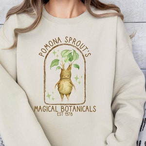 May include: A beige sweatshirt with a brown and green graphic of a plant creature with the text "Pomona Sprout's Magical Botanicals Est 1978"