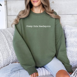 May include: A green sweatshirt with the text "Pretty Girls Needlepoint" printed in white on the front.