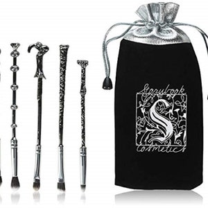 May include: Set of five black and silver makeup brushes shaped like wands, with a black velvet pouch with the text "Storylook Cosmetics" in white.