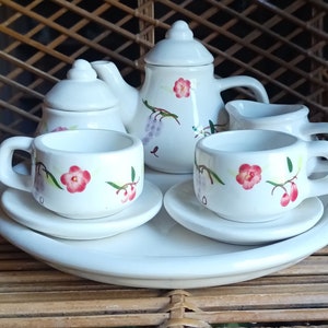 May include: A white tea set with floral designs. The set includes a teapot, creamer, sugar bowl, two cups, and two saucers.