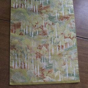 May include: A green, gold, and white table runner with a repeating pattern of vertical lines and abstract shapes. The runner has a gold fringe border.