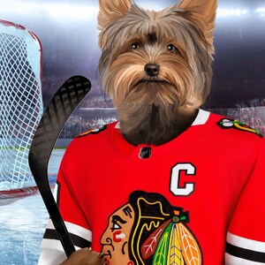 May include: A Yorkshire Terrier wearing a red hockey jersey with a black and white striped pattern, a black and white logo of a Native American head with feathers, and a white letter "C" on the front. The dog is holding a black hockey stick.