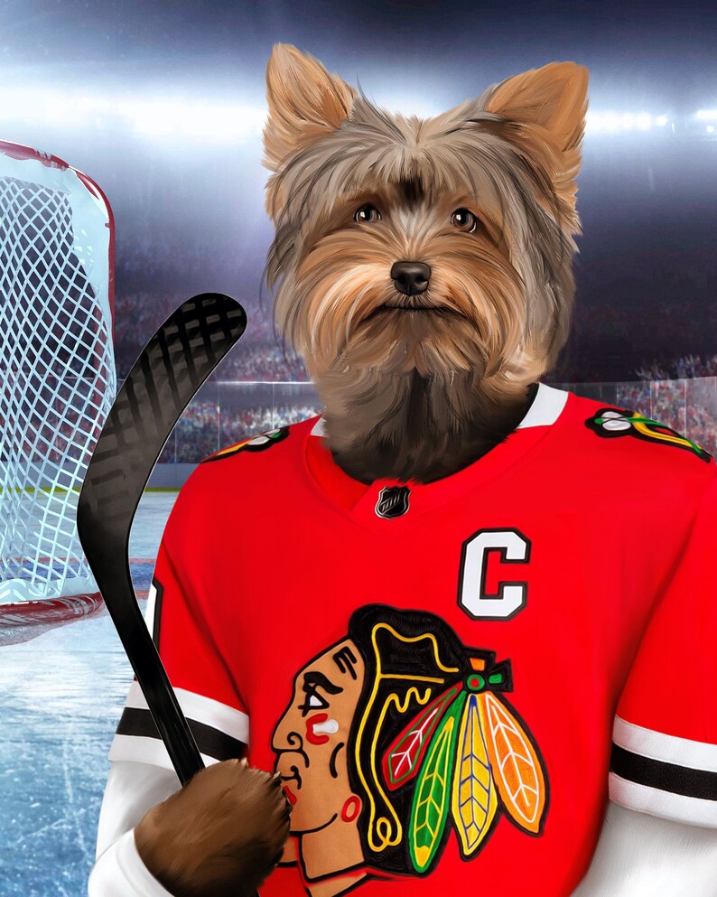 May include: A Yorkshire Terrier wearing a red hockey jersey with a black and white striped pattern, a black and white logo of a Native American head with feathers, and a white letter "C" on the front. The dog is holding a black hockey stick.