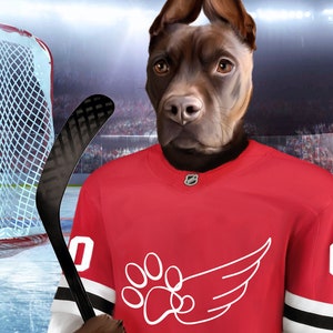 May include: A brown dog wearing a red hockey jersey with a white paw print and wing design. The dog is holding a black hockey stick.
