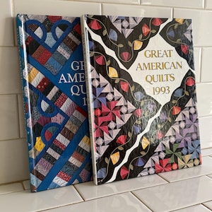 May include: Two hardcover books titled Great American Quilts 1993. The left book features a blue cover with a multi-colored patchwork quilt pattern. The right book has a black cover with a white center, floral vines, and a colorful quilt design.