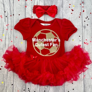 Baby girls red tutu romper with matching bow headband. Gold football design with white text saying Manchester's Cutest Fan. Manchester United, Man Utd, The Red Devils.