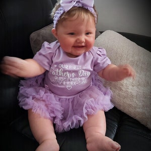 Baby Model wearing light purple short sleeve tutu romper with a matching bow and headband above. White love hearts design with lettering on the tutu romper saying Our First Father's Day Together Daddy & Daughter