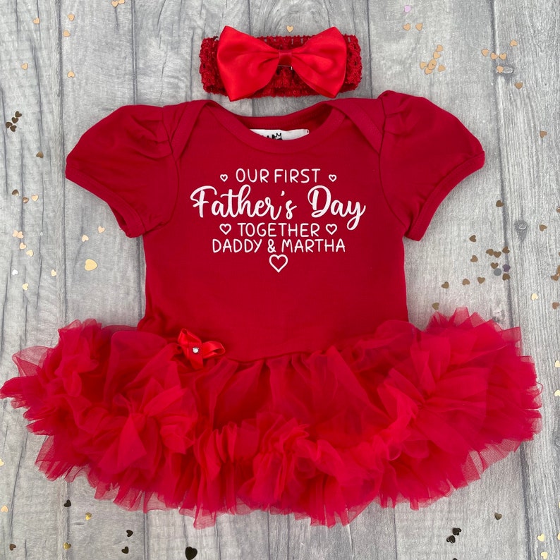 Red short sleeve tutu romper with a matching bow and headband above. White love hearts design with lettering on the tutu romper saying Our First Father's Day Together Daddy & Daughter