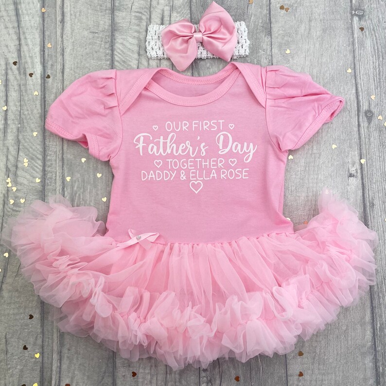 Light pink short sleeve tutu romper with a matching bow and headband above. White love hearts design with lettering on the tutu romper saying Our First Father's Day Together Daddy & Daughter