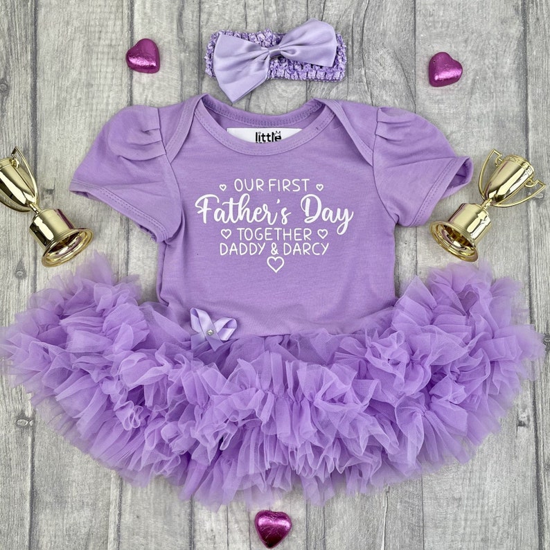 Light purple short sleeve tutu romper with a matching bow and headband above. White love hearts design with lettering on the tutu romper saying Our First Father's Day Together Daddy & Daughter