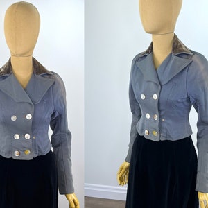May include: A cropped, double-breasted jacket in a light blue color with a velvet collar. The jacket has four large, decorative buttons.