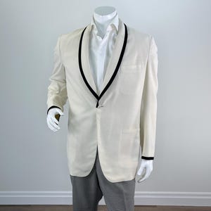 May include: Cream-colored blazer with black trim on the lapels and cuffs. The blazer is paired with black and white checkered pants and a white dress shirt. The outfit is displayed on a mannequin.