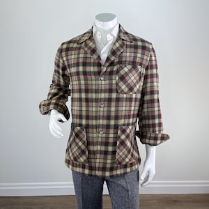 May include: A plaid jacket in beige, red, gray, and brown, displayed on a mannequin. The jacket has a collared neckline, button closures, and two front pockets. The sleeves are rolled up, revealing the lining. The mannequin is also wearing a white shirt and gray pants.