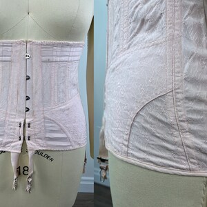 May include: A pale pink corset with a lace pattern and a hook and eye closure in the back. The corset has a boned structure and garter straps at the bottom. The words "COLLAR" and "SHOULDER" are written on the bottom of the corset.