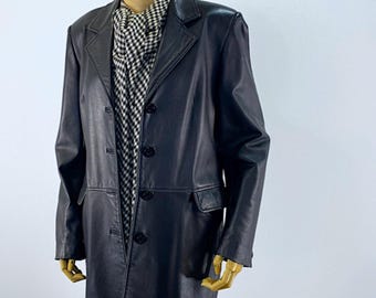 May include: A long black leather coat featuring a notched lapel, four front buttons, and two flap pockets. The coat is worn over a black and white houndstooth patterned garment that is visible at the neckline and extending below the coat hem.