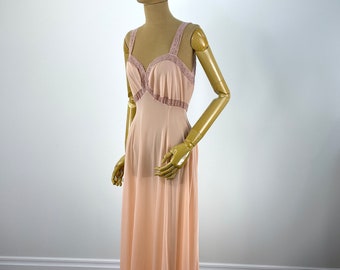 May include: A long, peach-colored slip dress with delicate lace trim at the neckline and bust. The dress is made of a sheer, lightweight fabric and has a flowing silhouette.
