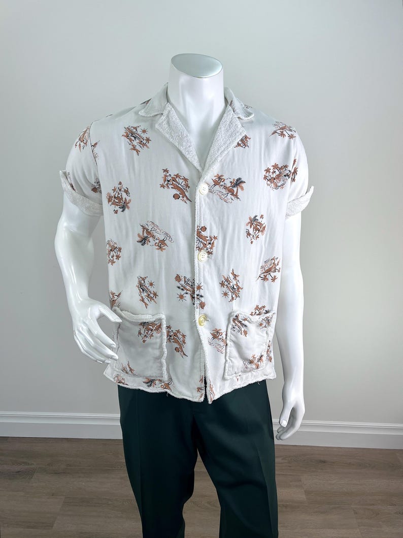 May include: White short-sleeved shirt with a brown and tan floral pattern. The shirt has a collar, two front pockets, and button closures. The sleeves are rolled up. The shirt is displayed on a mannequin.