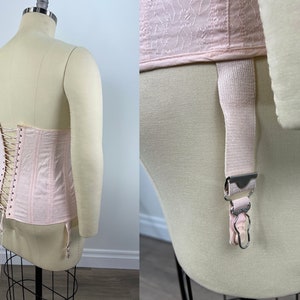 May include: A pink satin corset with a lace-up back and garter straps. The corset is on a white mannequin.