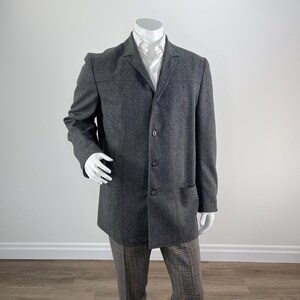 May include: A charcoal gray blazer with a three-button closure and two front pockets. The blazer is paired with plaid trousers. The mannequin is wearing a white collared shirt underneath the blazer.