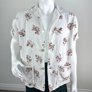 May include: White short-sleeved shirt with a brown and tan tropical print. The shirt has two front pockets and three gold-colored buttons. The collar and cuffs have a terry cloth texture.