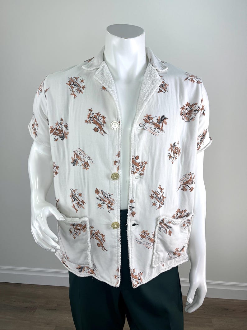 May include: White short-sleeved shirt with a brown and tan tropical print. The shirt has two front pockets and three gold-colored buttons. The collar and cuffs have a terry cloth texture.