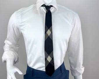 May include: A white dress shirt with a black and gray plaid tie. The tie is knotted and hangs down over the shirt. The shirt is paired with blue pants. The mannequin has a white head and arms.