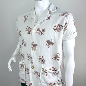 May include: White short-sleeved shirt with a brown and tan tropical print. The shirt has two front pockets, a collar, and two buttons. The cuffs and collar are trimmed with a white terry cloth material. The shirt is displayed on a white mannequin.