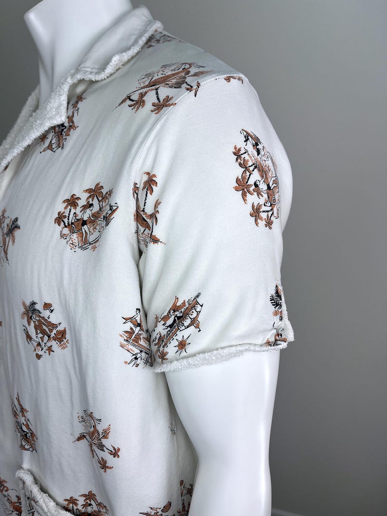 May include: White short-sleeved shirt with a brown and black tropical print featuring palm trees and figures. The shirt has a frayed collar and sleeve edges, giving it a casual look.