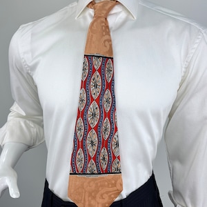 May include: A tan silk tie with a geometric pattern in shades of red, blue, and beige. The pattern features repeating circles and ovals.