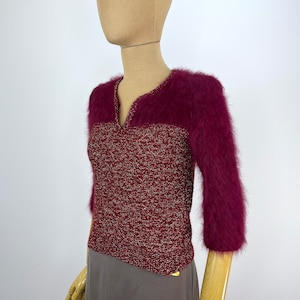 May include: A burgundy sweater with a V-neck and three-quarter sleeves. The top section and sleeves are made of a fuzzy material, while the body has a textured knit design. The sweater is displayed on a mannequin.