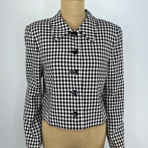 May include: A black and white houndstooth patterned blazer with a collared neckline and button closure.