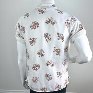 May include: White short-sleeve shirt with a brown and tan pattern. The shirt has a button-down front and a collar. The sleeves are cuffed. The shirt is displayed on a mannequin.