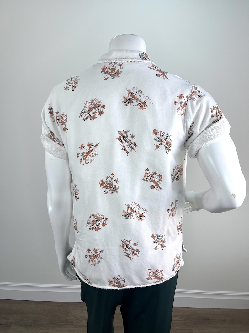 May include: White short-sleeve shirt with a brown and tan pattern. The shirt has a button-down front and a collar. The sleeves are cuffed. The shirt is displayed on a mannequin.