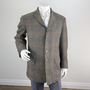 Puede incluir: Un blazer a cuadros marrón, negro y beige con tres botones y dos bolsillos delanteros. El blazer se usa sobre una camisa blanca con cuello y pantalones grises. La chaqueta se exhibe en un maniquí.