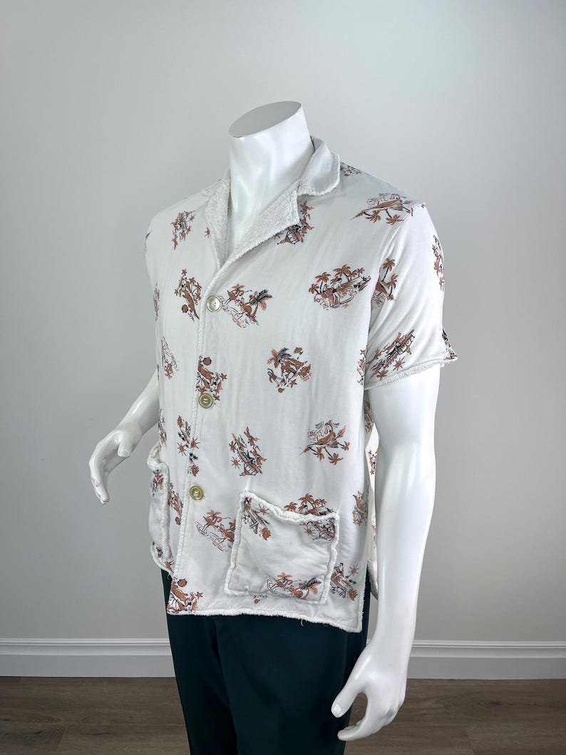 May include: White short-sleeved shirt with a brown and tan tropical print. The shirt has a collar, two front pockets, and two buttons. The edges of the shirt have a frayed design.
