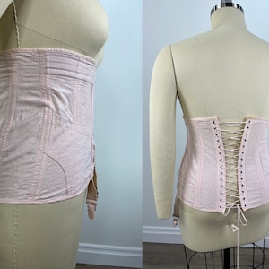 May include: A pale pink corset with a lace-up back and garter straps. The corset is made of a soft, lightweight fabric and has a vintage style.