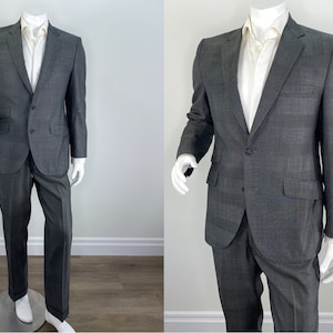 May include: A gray two-piece suit with a single-breasted jacket and a button closure. The jacket has a notch lapel and flap pockets. The pants have a straight leg.