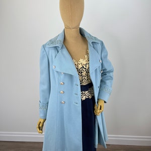 May include: A light blue coat with a double breasted closure and silver buttons. The coat has embroidered details on the collar and cuffs.