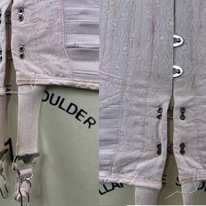 May include: A pair of pink garters with metal clasps and elastic straps. The garters are attached to a pink corset with white elastic bands and metal hooks.