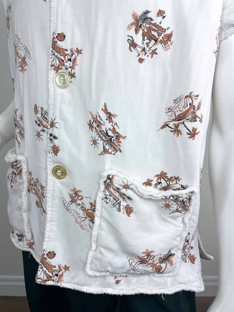 May include: White vest with a brown and black tropical print featuring palm trees and figures. The vest has two front pockets and two large buttons. The edges of the vest and pockets have a frayed design.