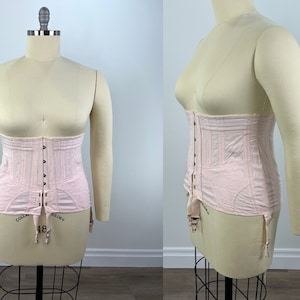 May include: A pink corset with a front closure and adjustable straps. The corset has a boned structure and is designed to cinch the waist.