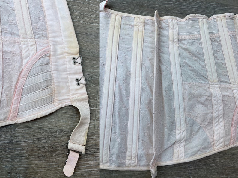 May include: A white corset with pink accents and a lace pattern. The corset has a hook and eye closure in the front and a lace-up back. The corset has a garter strap on the side.
