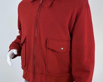 May include: A vibrant red bomber jacket featuring a classic fold-down collar, a full-length front zip, and two large patch pockets with snap-button flaps. The garment includes ribbed knit cuffs and a ribbed hem, worn over a plaid shirt and trousers.