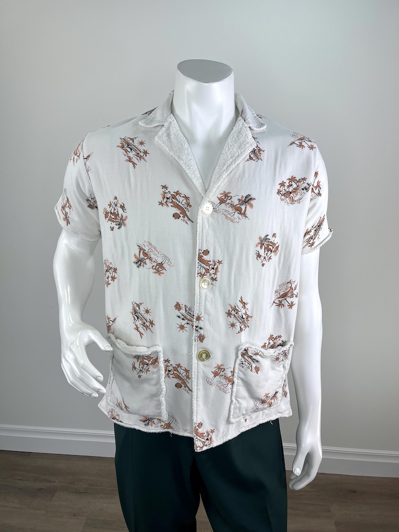 May include: White short-sleeved shirt with a brown and tan tropical print. The shirt has two front pockets and a button-up closure. The collar and pocket edges have a textured trim.