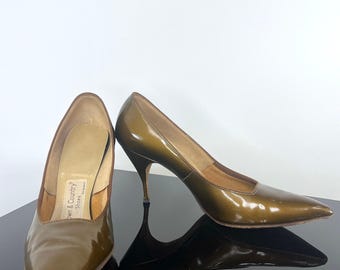 May include: A pair of olive green patent leather pumps with a pointed toe and a slim stiletto heel. The interior insole features a white label with the text Town & Country Shoes printed in black. The shoes have a glossy finish and a low-cut vamp.
