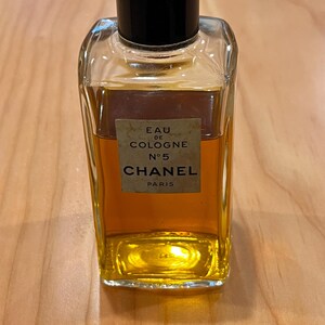 Puede incluir: Una botella rectangular de vidrio de Chanel No. 5 Eau de Cologne. La botella tiene una tapa negra y una etiqueta con el nombre de la marca y los detalles del producto. El l&iacute;quido interior es de color &aacute;mbar.