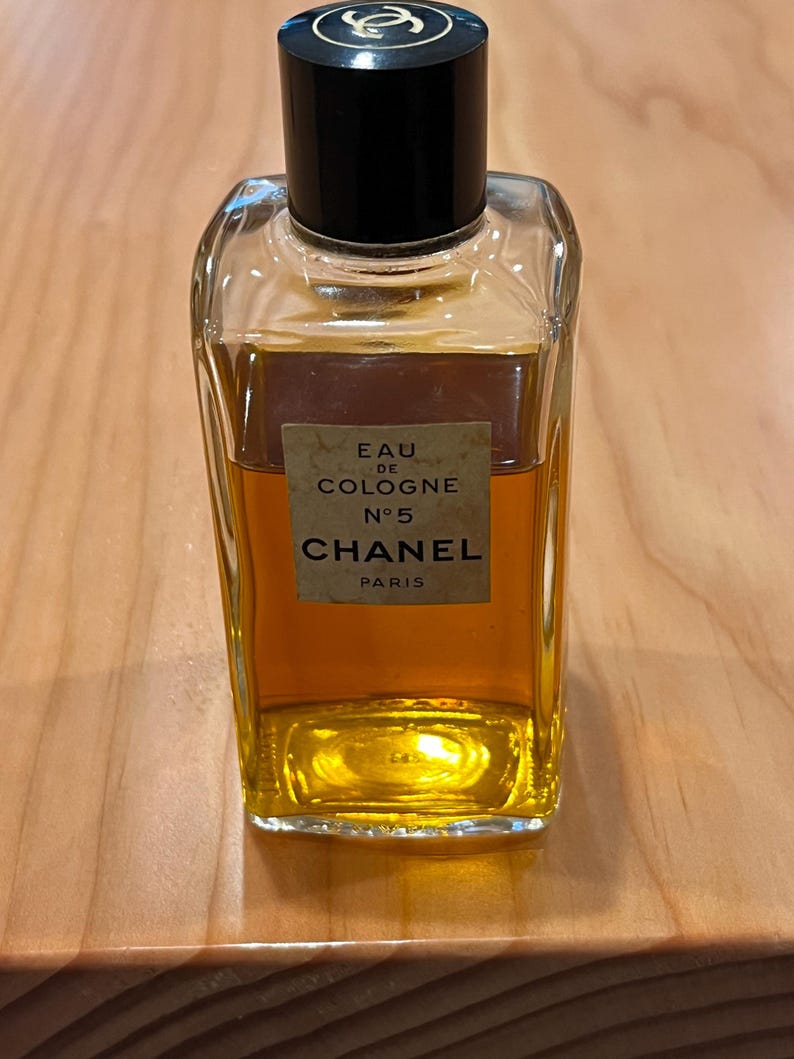 Puede incluir: Una botella rectangular de vidrio de Chanel No. 5 Eau de Cologne. La botella tiene una tapa negra y una etiqueta con el nombre de la marca y los detalles del producto. El l&iacute;quido interior es de color &aacute;mbar.