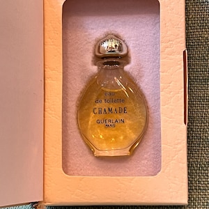 May include: A miniature perfume bottle of "Chamade" eau de toilette by Guerlain, Paris. The bottle is pear-shaped with a silver cap, set in a peach-colored box. The liquid inside is golden.