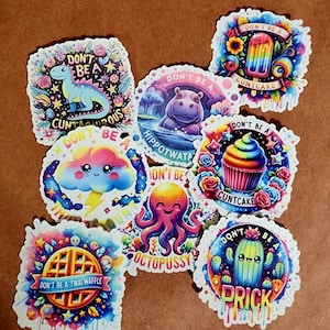 May include: A collection of colorful, round stickers with various designs and text. The stickers feature illustrations of a dinosaur, hippo, cloud, octopus, waffle, cactus, cupcake, and popsicle. Each sticker has the phrase "Don't Be A" with a humorous word.
